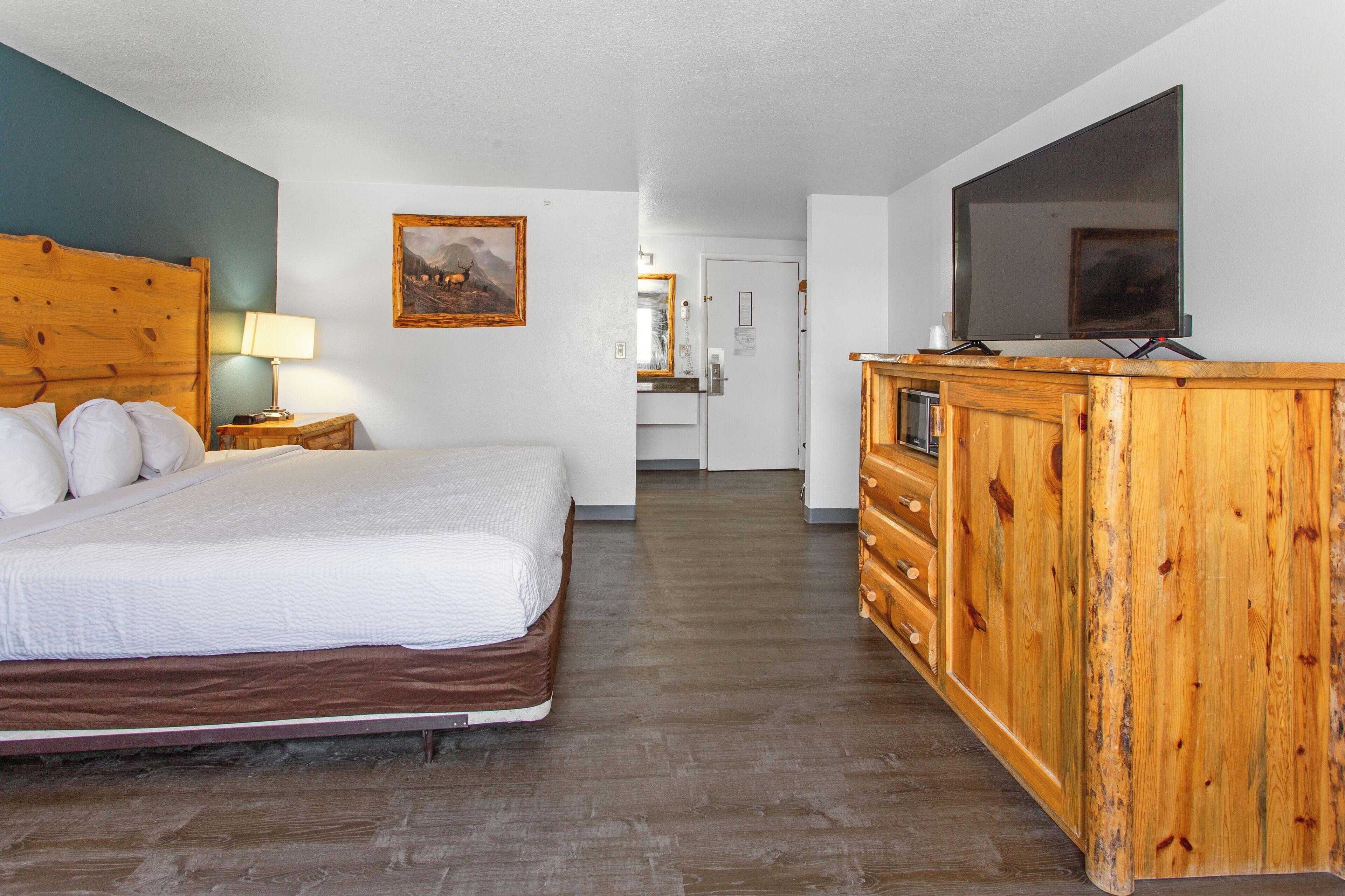 Een hotelkamer met een houten bed, een houten dressoir en een televisie op een standaard.