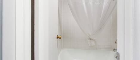 Une salle de bain avec une baignoire blanche, une serviette suspendue sur le bord et un rideau de douche.