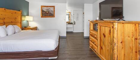 Habitación de hotel con cama de cabecera de madera, cómoda de madera con televisor de pantalla plana y un cuadro en la pared.