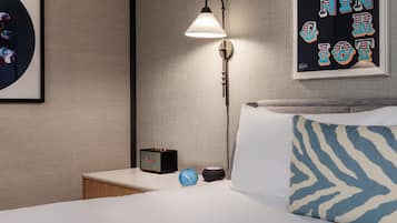 Habitación de hotel ordenada con una cama, una mesita de noche, una lámpara, un reloj y un cuadro en la pared.