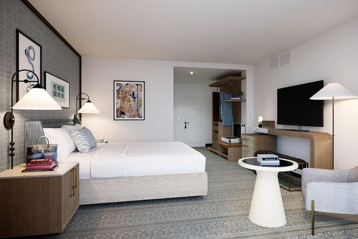 A hotel room with a bed, bedside tables, a TV, a chair, and a small table.