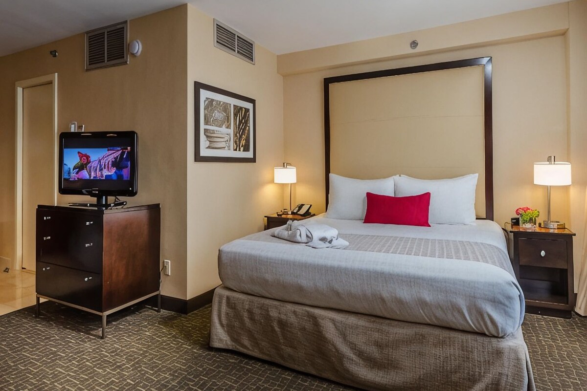 A hotel room with a large bed, a television, a dresser, and two bedside tables with lamps.