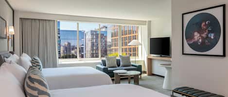 Habitación de hotel con dos camas, un sofá, un televisor y un ventanal con vistas a la ciudad.