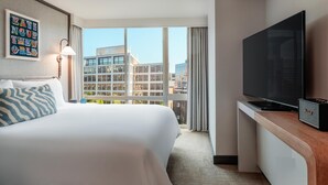 A hotel room with a large bed, a flat-screen TV, a desk with a speaker, and a view of buildings through large windows. - The Beacon at Embassy Row, WorldHotels Distinctive (Washington)