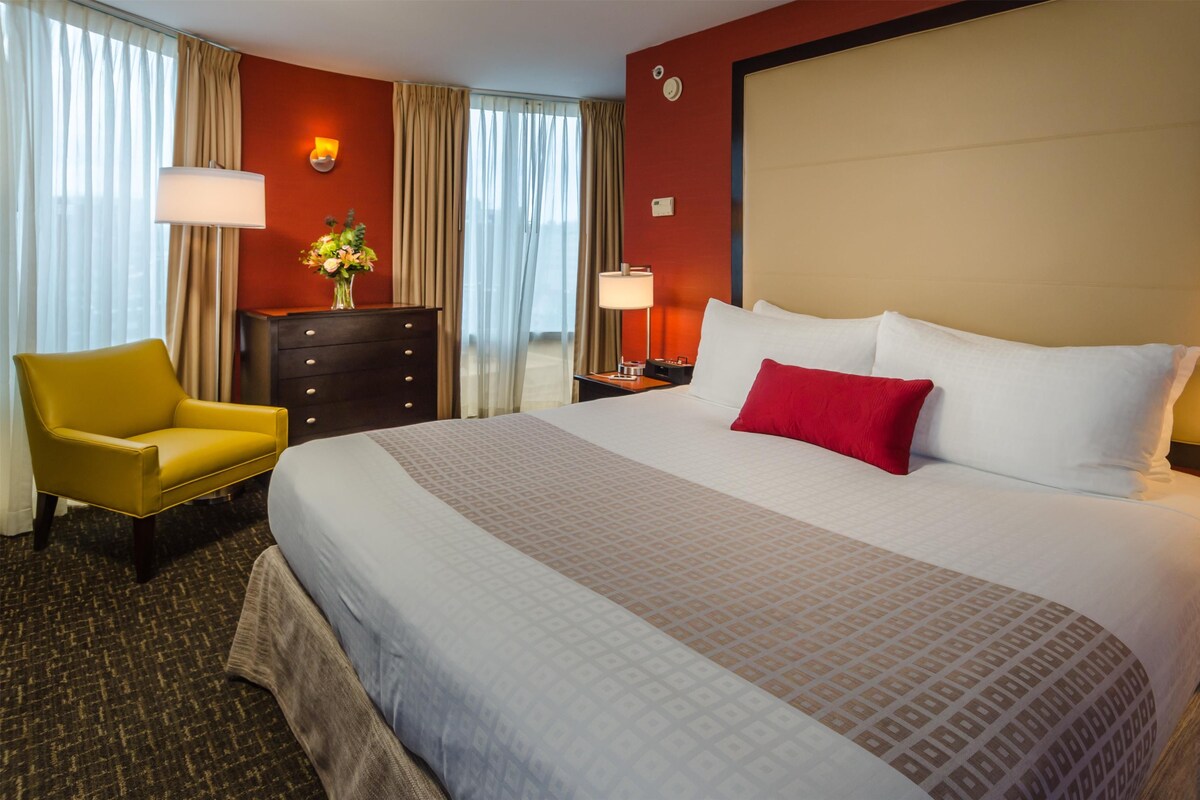 A hotel room with a large bed, a yellow armchair, a dresser, and a vase of flowers.