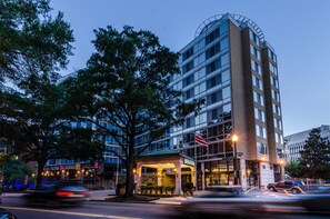 Een hotel met meerdere verdiepingen, een glazen gevel, een overdekte ingang en een vlag.