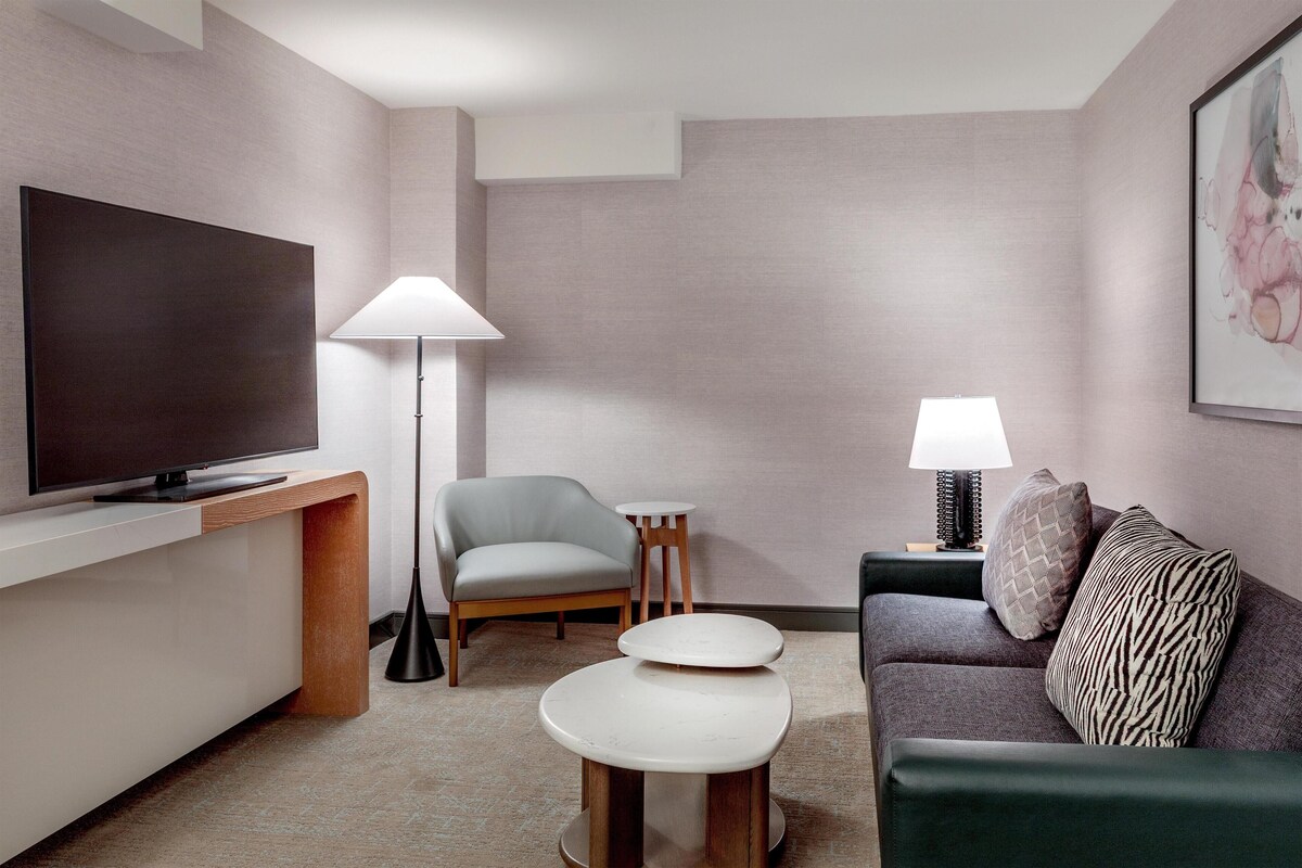 A modern living room with a flat-screen TV, a sofa, a chair, a small table, and two lamps.
