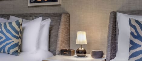 A neatly made bed with patterned pillows, a bedside table with a lamp, a small speaker, and a decorative wall piece.