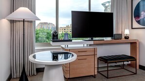 A hotel room with a large TV, a desk with a computer, a small table, a bench, and a window with curtains. - The Beacon at Embassy Row, WorldHotels Distinctive (Washington)