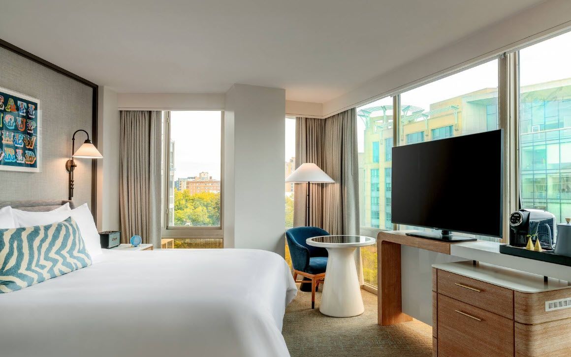 A hotel room with a bed, a desk, a chair, a television, and a window with a city view.