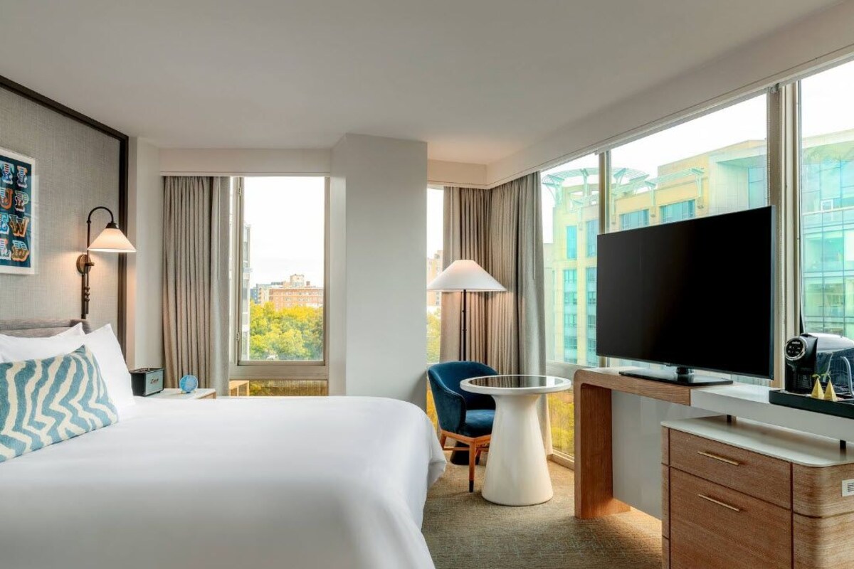 A hotel room with a bed, a desk, a chair, a television, and a window with a city view.