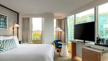 A hotel room with a bed, a desk, a chair, a television, and a window with a city view.