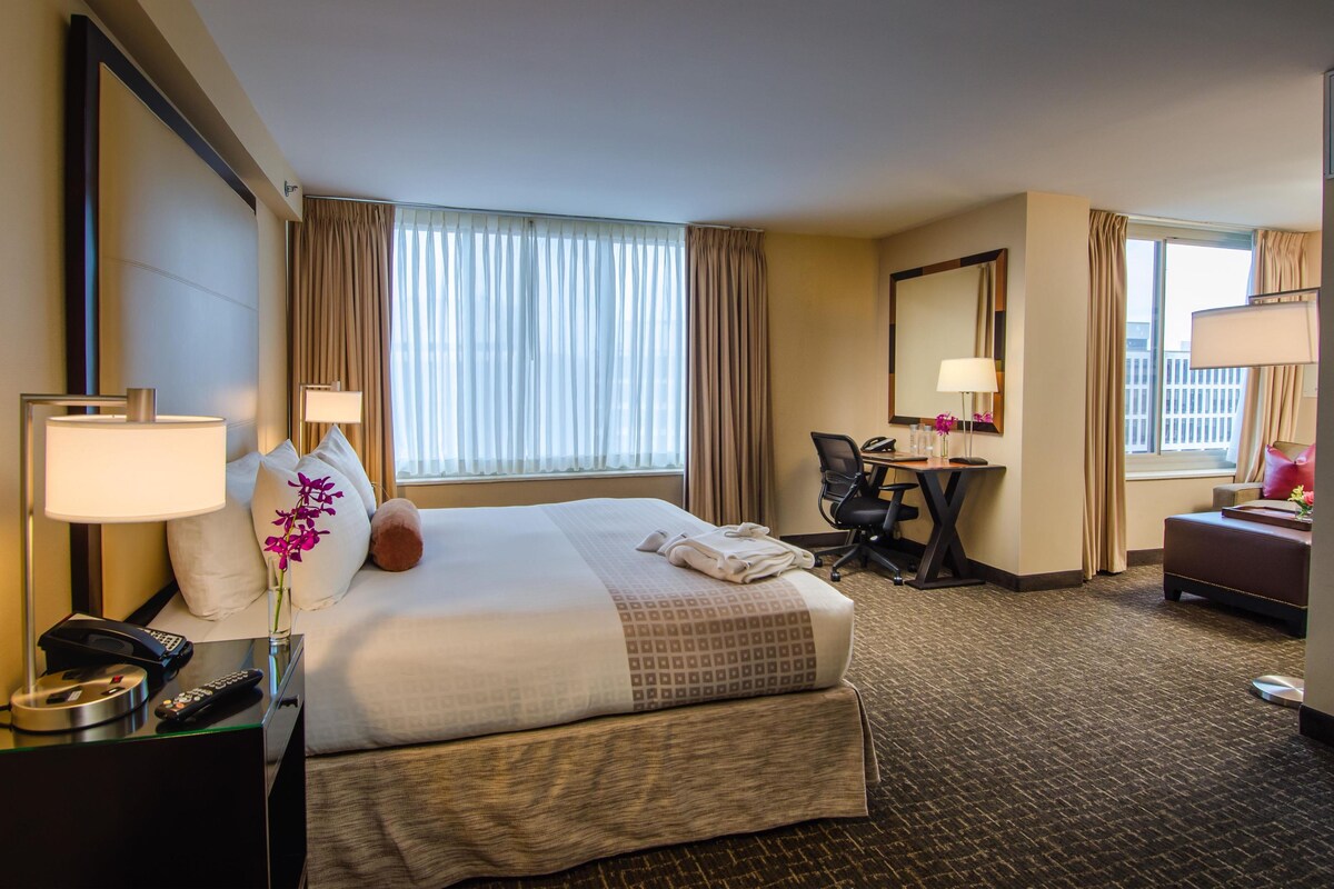 A hotel room with a large bed, a desk, a chair, and a bathroom mirror.