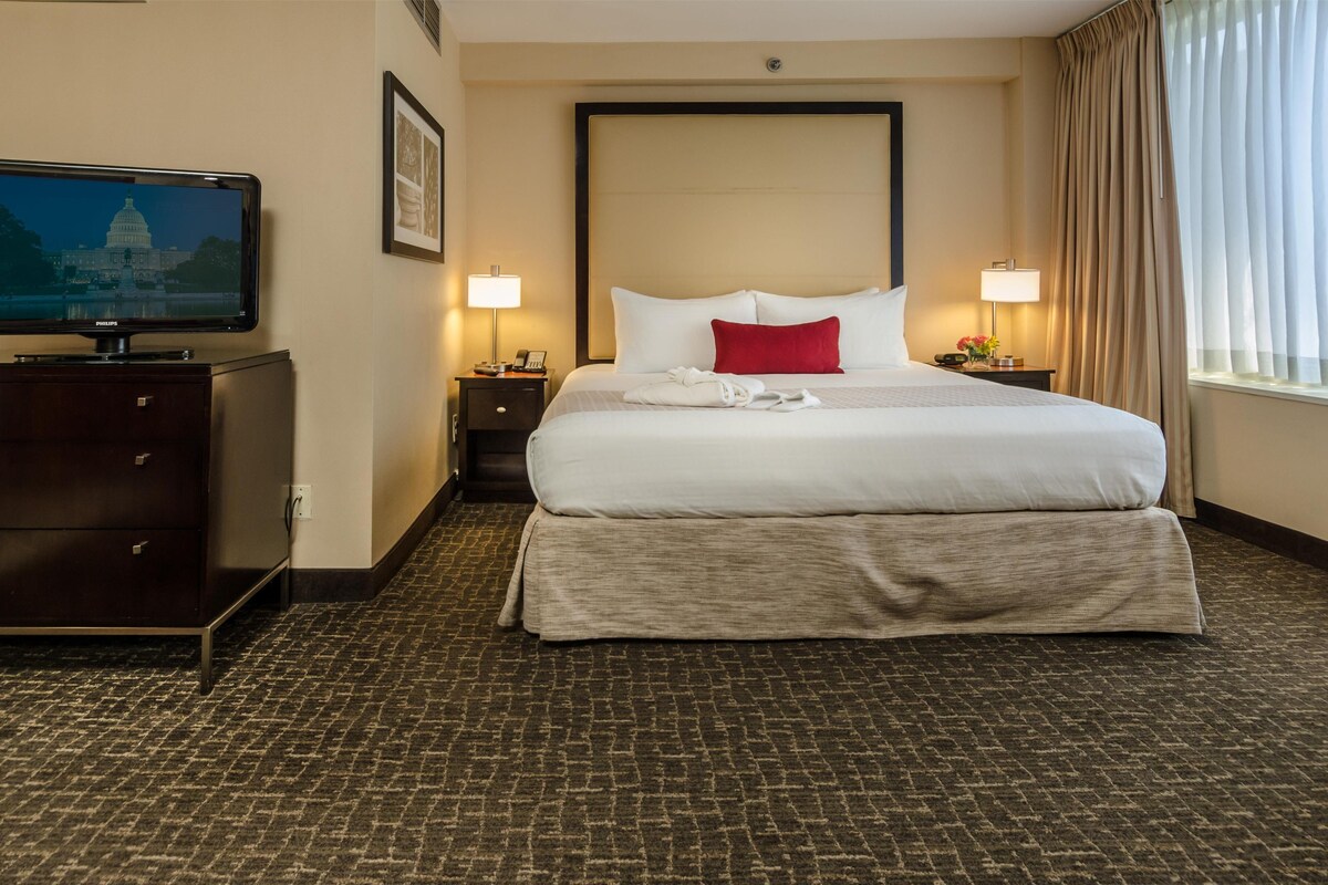 A hotel room with a large bed, a television on a dresser, and a view of the Capitol building.