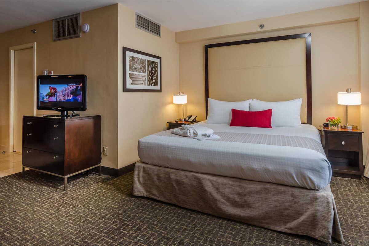 A hotel room with a large bed, a television on a dresser, and two bedside lamps.