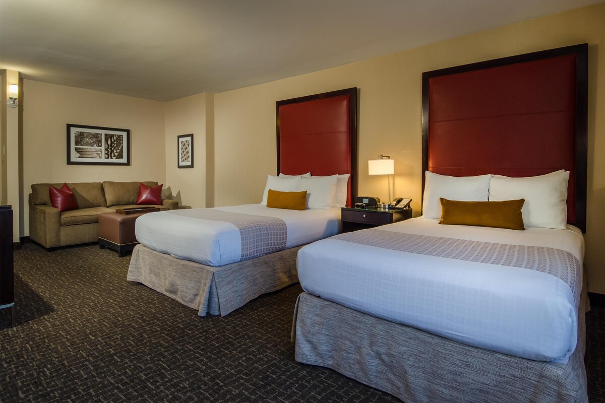 A hotel room with two beds, a sofa, and a desk.