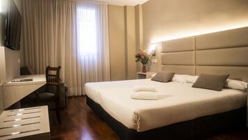 Una habitación de hotel moderna con una cama grande, un escritorio, una silla y un televisor montado en la pared.