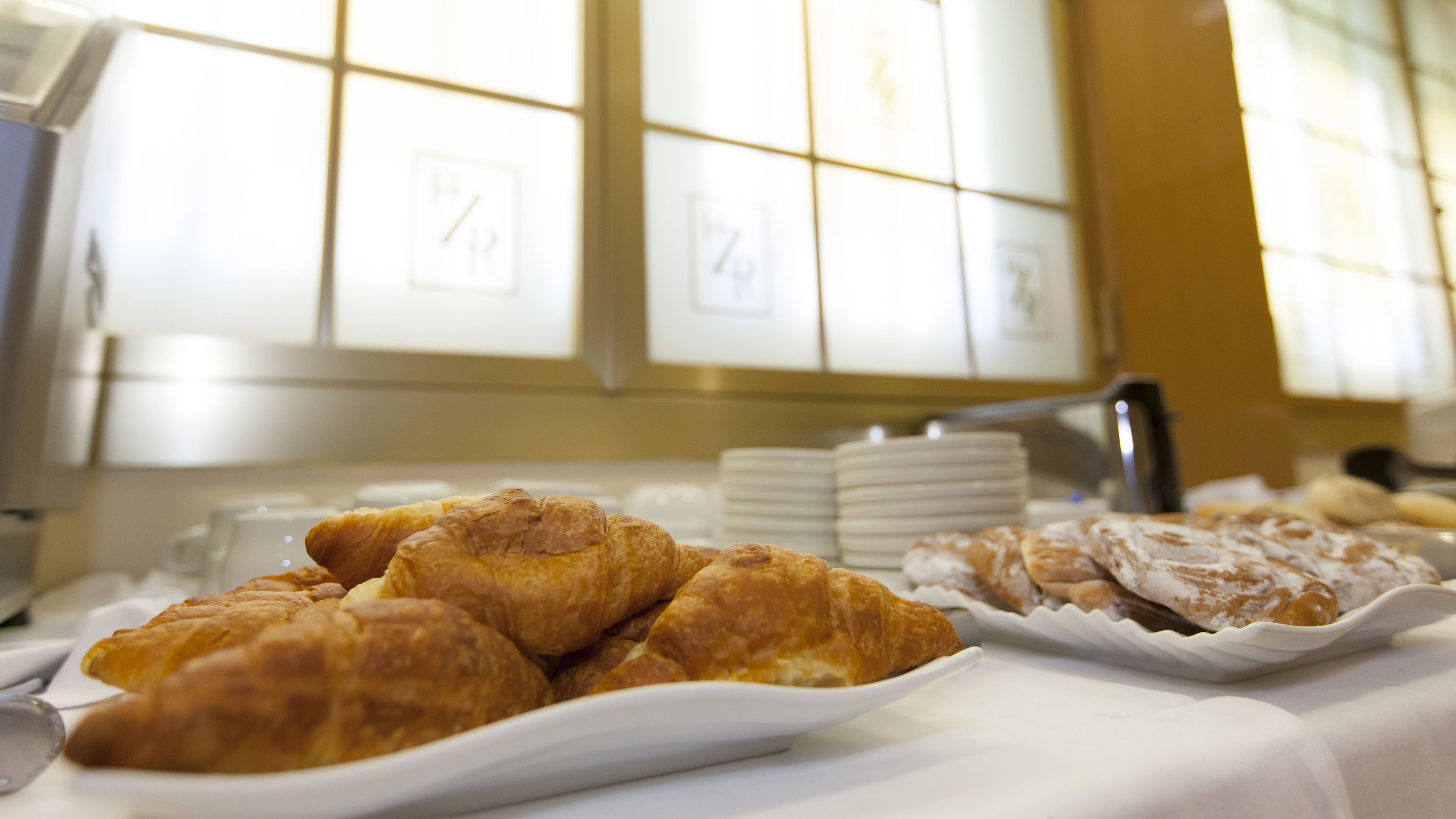 Una mesa de buffet con diversos pasteles y una pila de platos blancos.