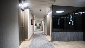 A long, narrow hallway with a carpeted floor, doors on both sides, and a fire extinguisher mounted on the wall. - B&B Hotel Zaragoza Royal (Zaragoza)