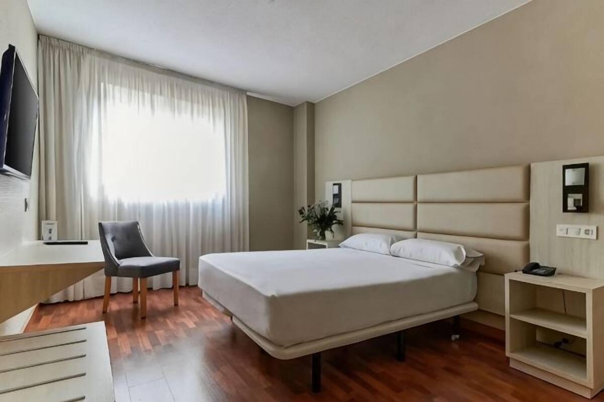 Een hotelkamer met een bed, een bureau, een stoel, een televisie en een raam met gordijnen.