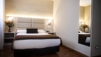 Habitación de hotel con una cama grande, mesitas de noche, un espejo y una lámpara fijada a la pared.
