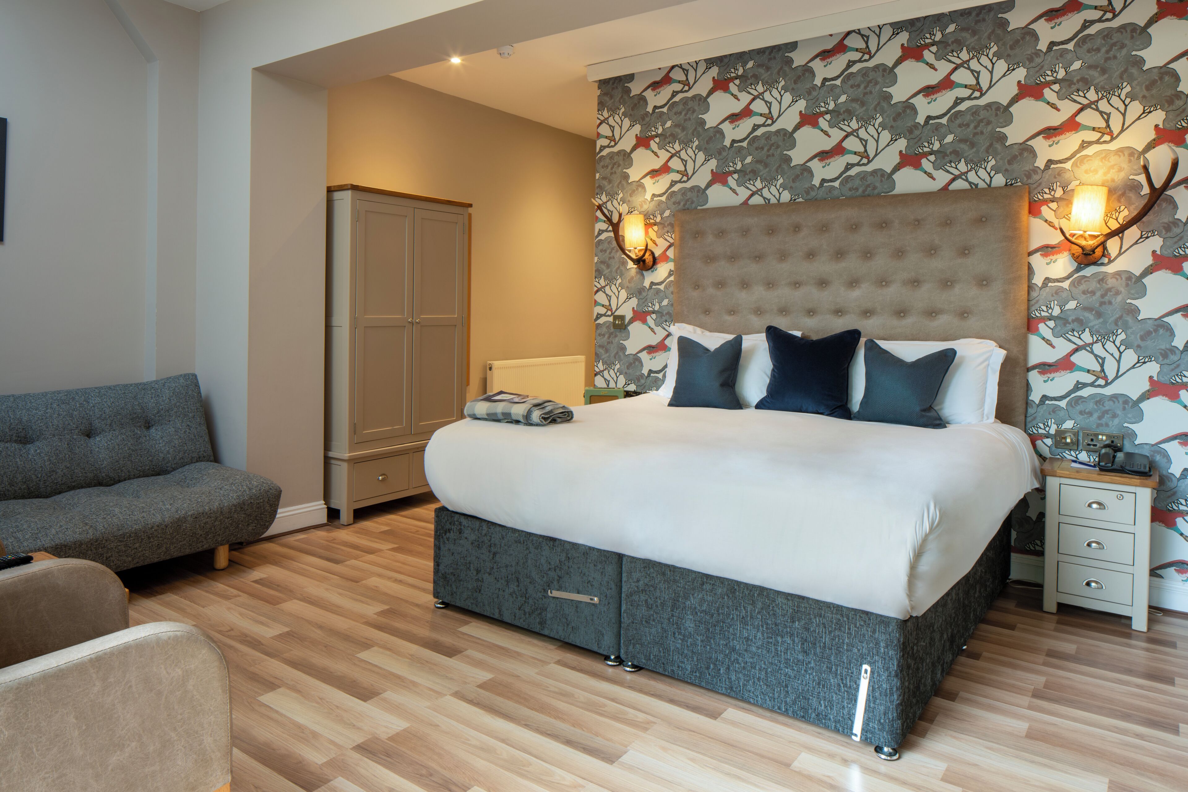 Ein Schlafzimmer mit einem großen Bett, einem grauen Sofa, einem Kleiderschrank und einem Nachttisch mit Lampe.