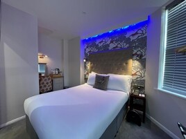 Un dormitorio con cama, mesita de noche, teléfono en la pared y ventana con persianas.