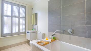 Un baño moderno con bañera, inodoro y ventana con persianas.