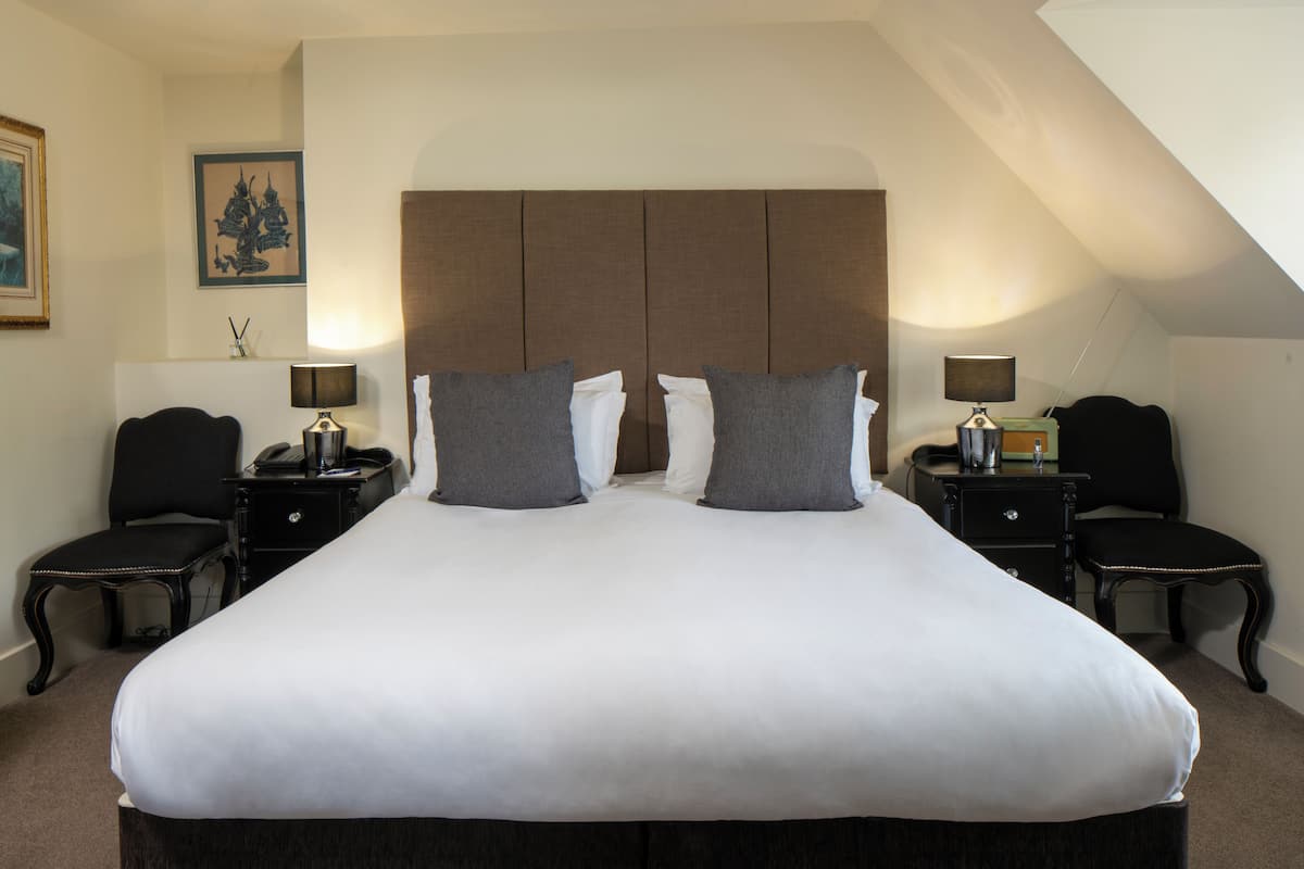 A large bed with a headboard, two bedside tables with lamps, and two chairs.