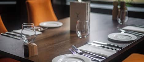 A dining table set with plates, cutlery, and glasses, with a wooden block and a vase on the table.