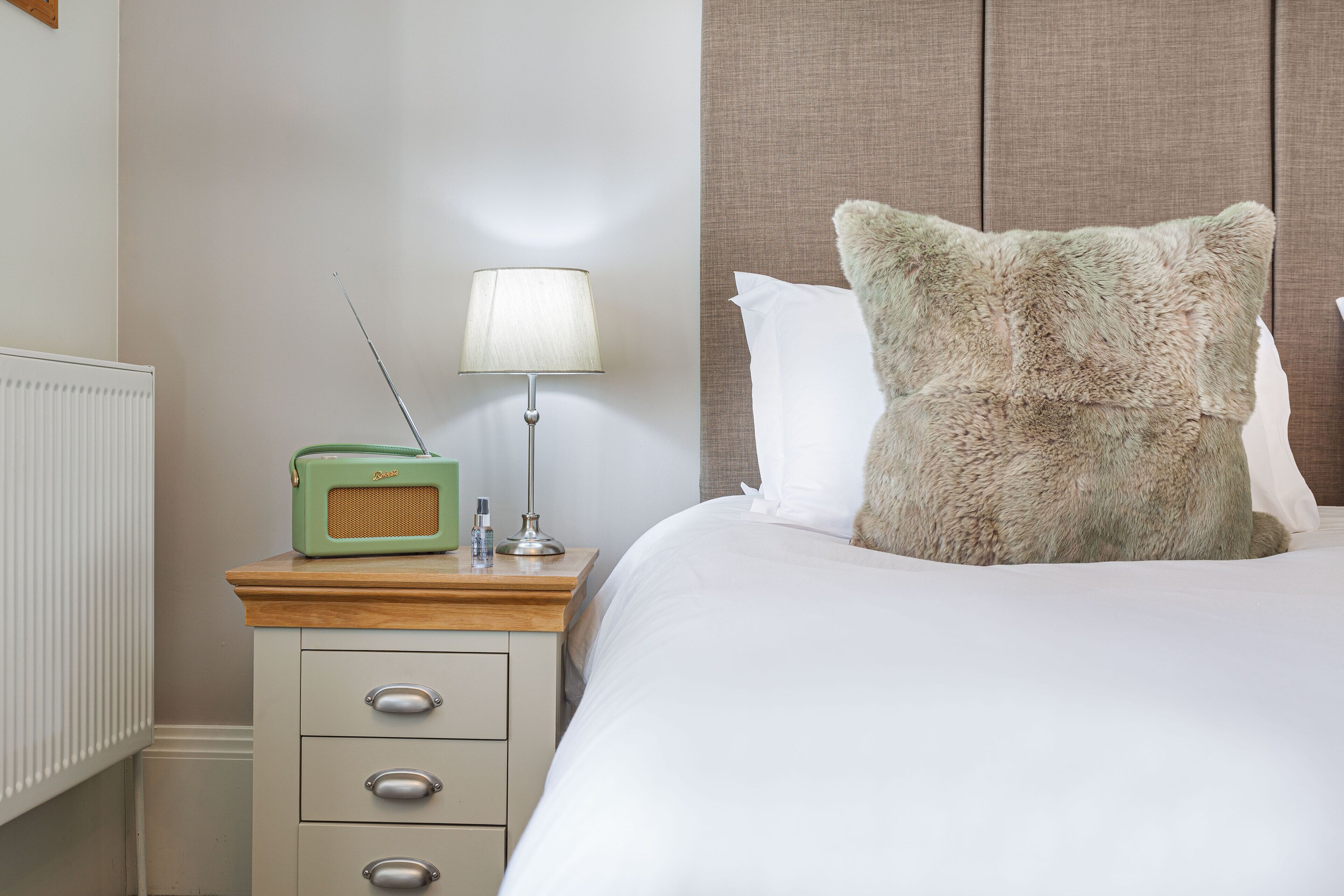 A neatly made bed with a fluffy pillow, a bedside table with a lamp, and a vintage radio.