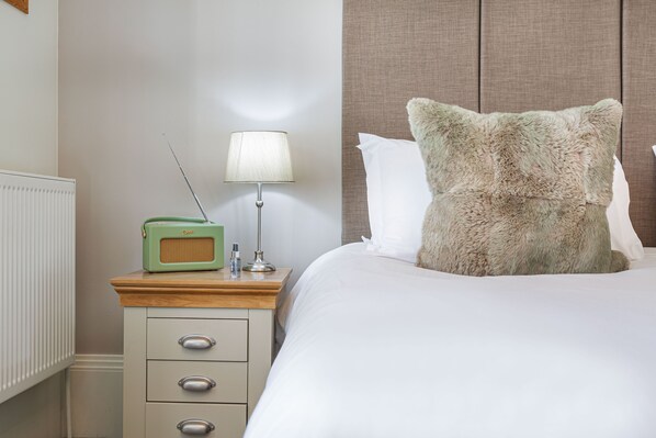 A neatly made bed with a fluffy pillow, a bedside table with a lamp, and a vintage radio.
