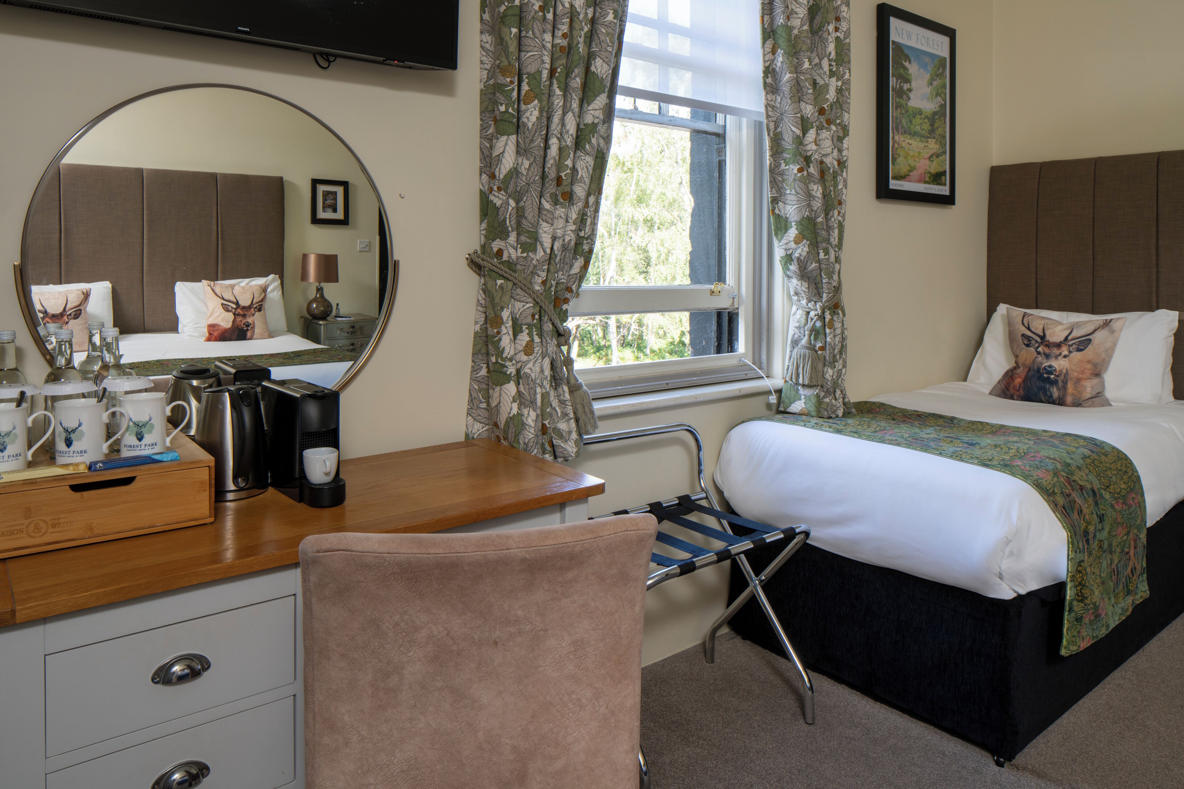 A hotel room with a bed, a desk with a mirror, a chair, a window with curtains, and a picture on the wall.