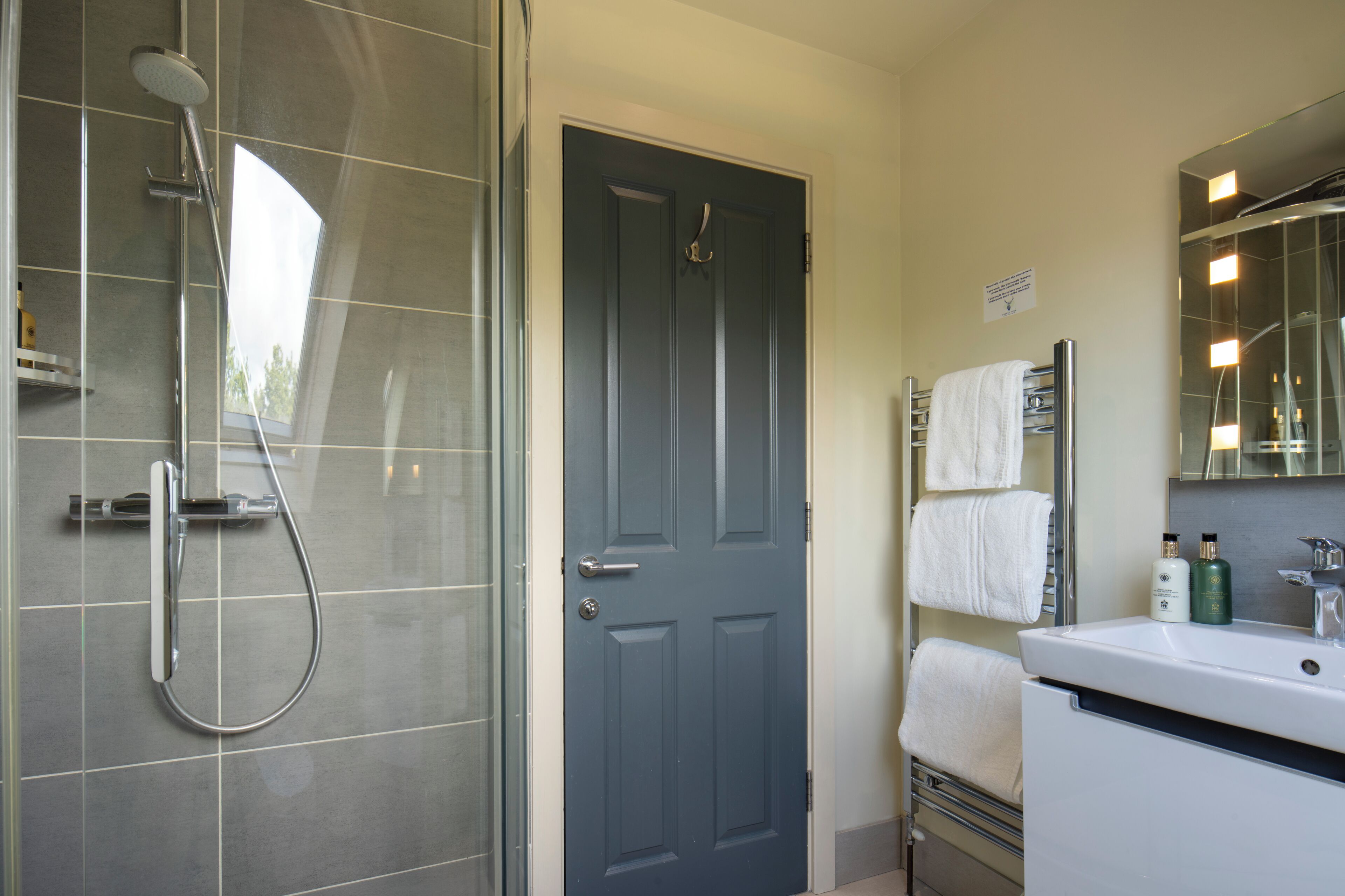 A bathroom with a shower, a door, a sink with toiletries, and a towel rack.