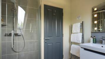 A bathroom with a shower, a door, a sink with toiletries, and a towel rack.