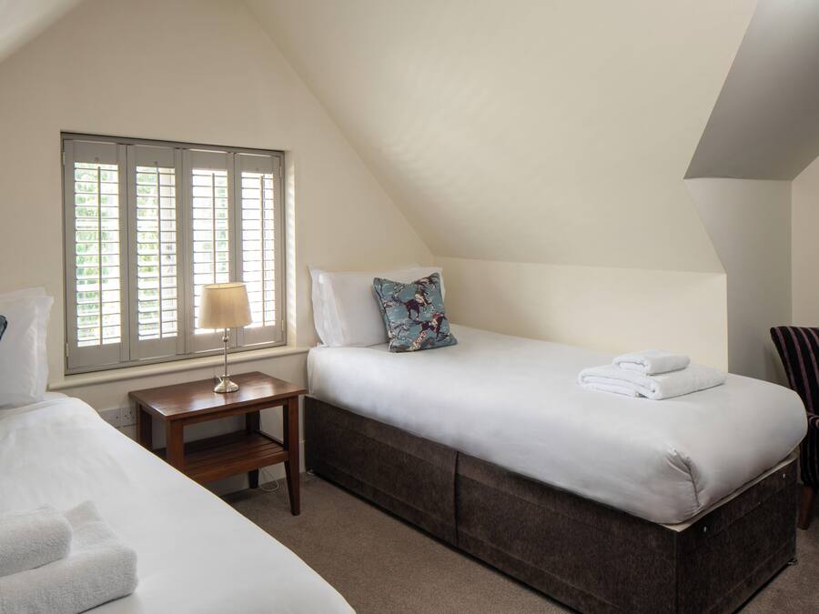 A bedroom with a bed, a bedside table with a lamp, a window with blinds, and a chair.