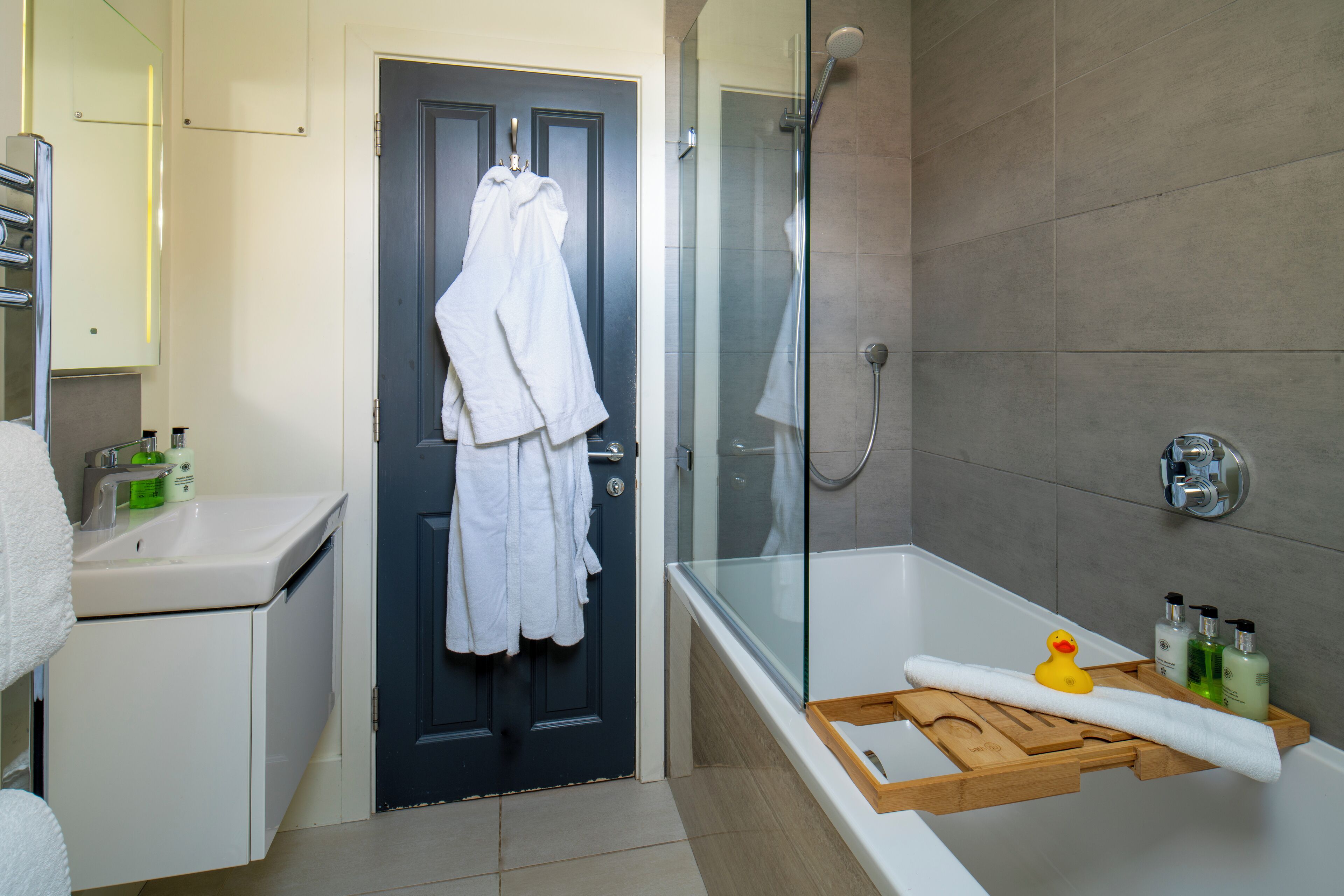 Un baño con bañera, cabina de ducha de vidrio, lavabo blanco y una puerta con dos toallas blancas colgadas.