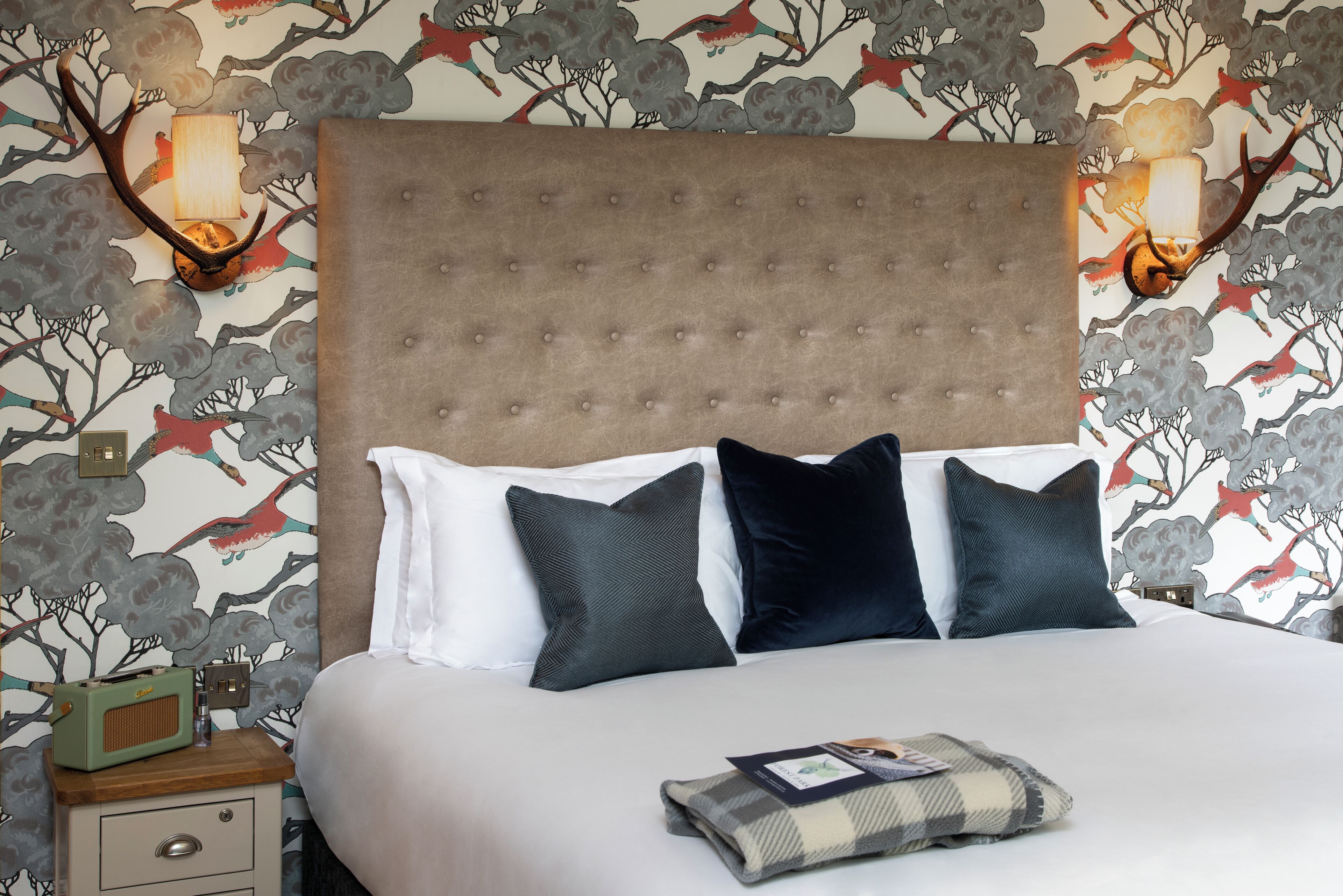 A neatly made bed with a tufted headboard, two bedside tables, and a wall with a floral wallpaper design.