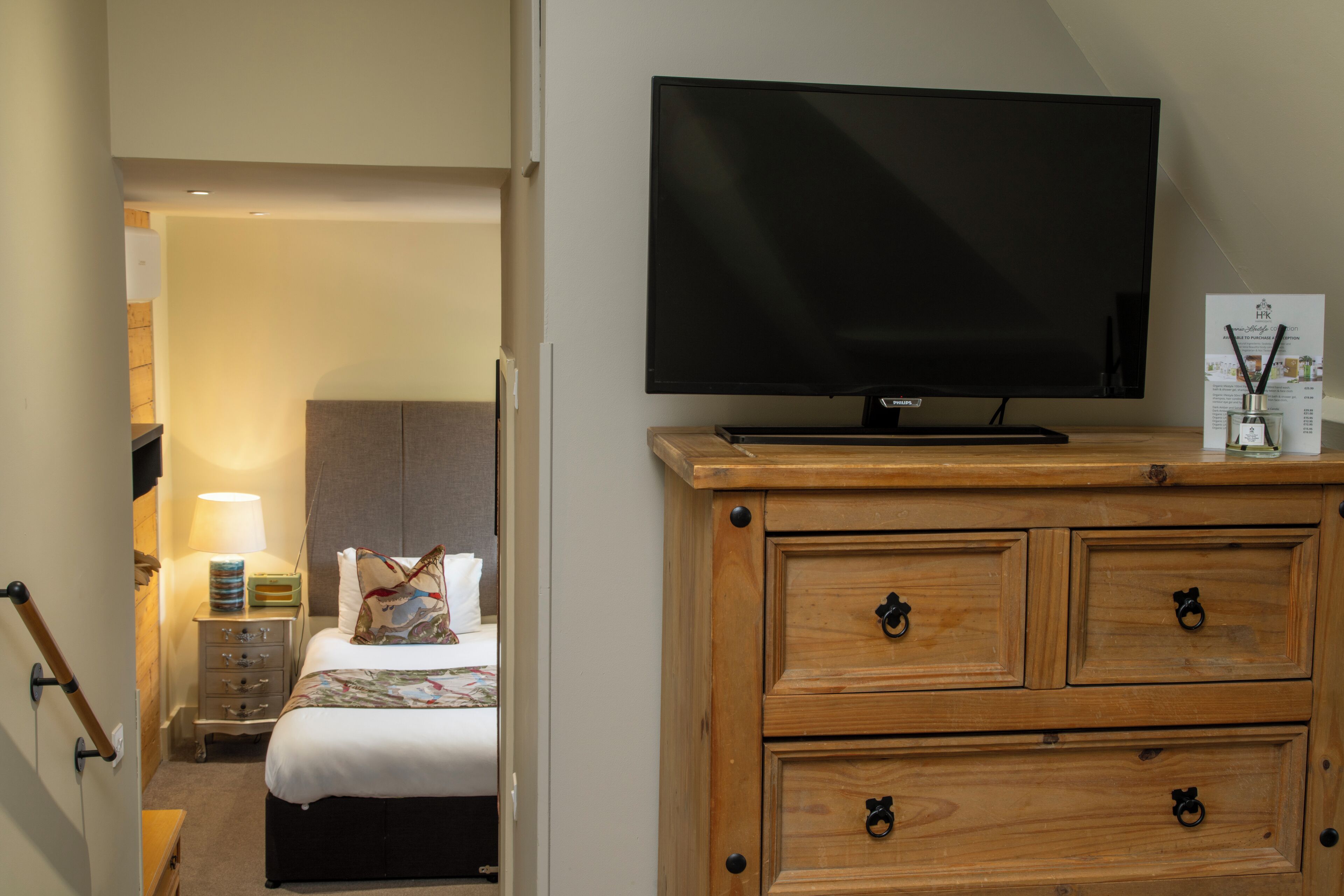 A hotel room with a television on a wooden dresser, a bed with a floral bedspread, and a nightstand with a lamp.