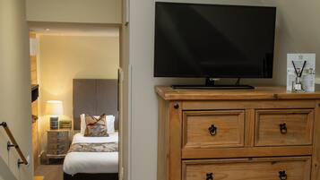 A hotel room with a television on a wooden dresser, a bed with a floral bedspread, and a nightstand with a lamp.