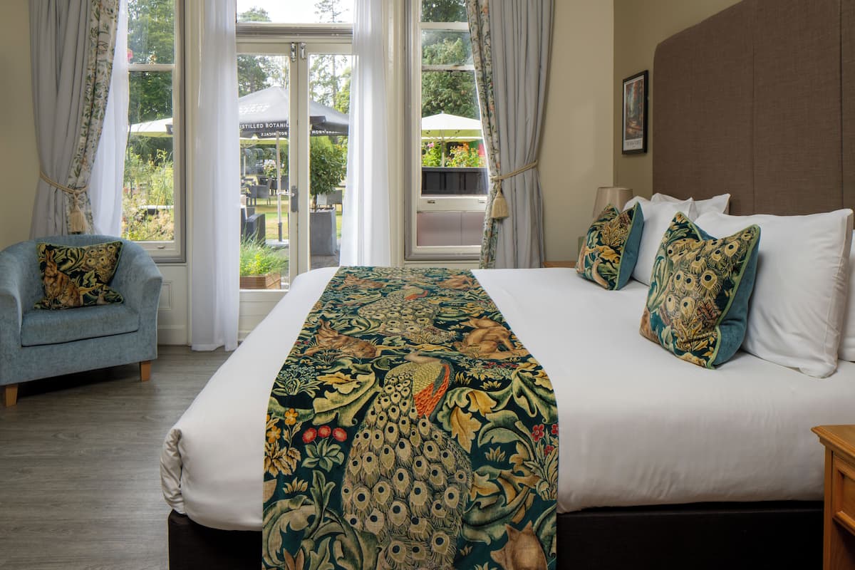 A hotel room with a large bed, a chair, and a view of the garden through the window.