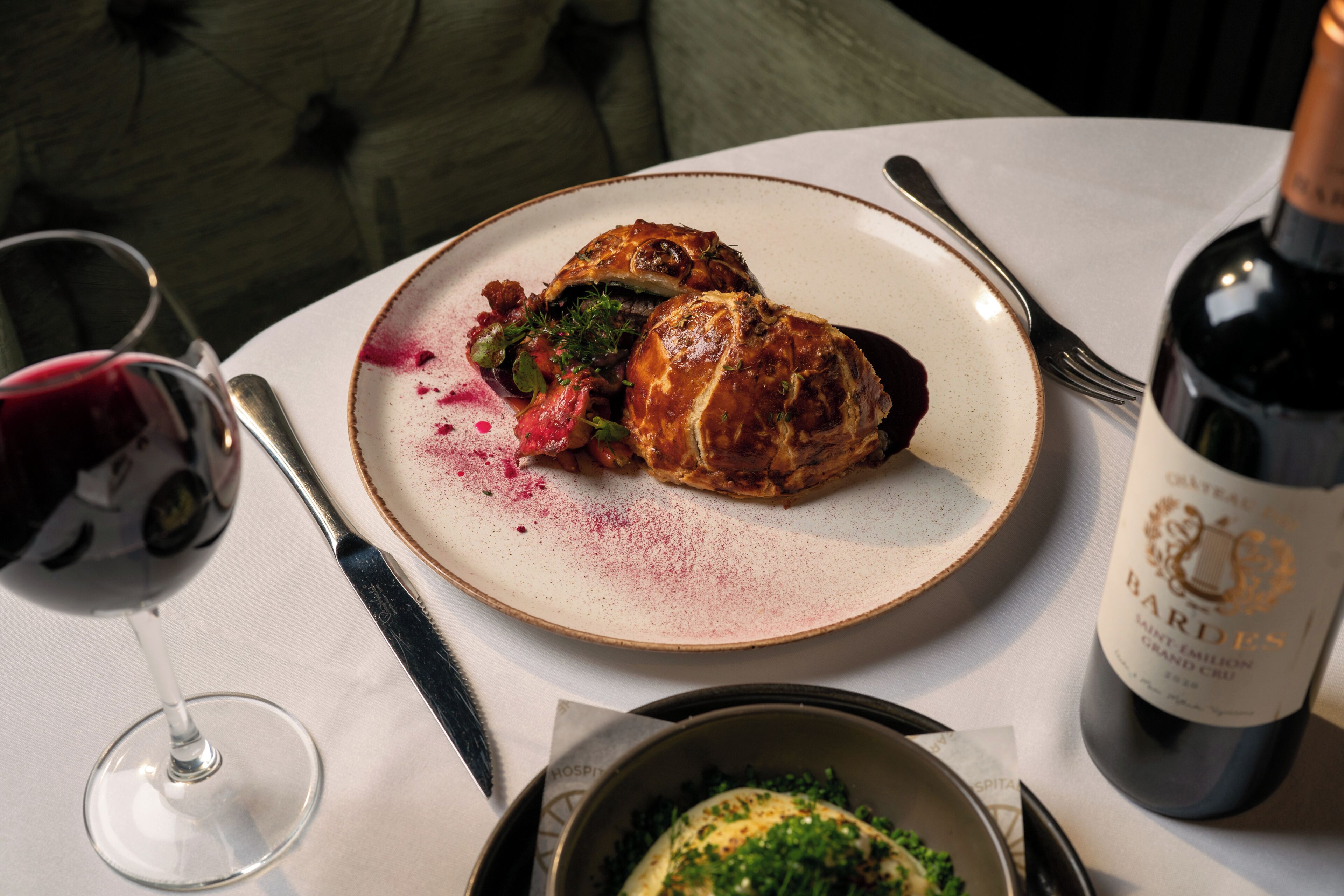 A dining table with a plate of food, a wine glass, a bottle of wine, and a fork.