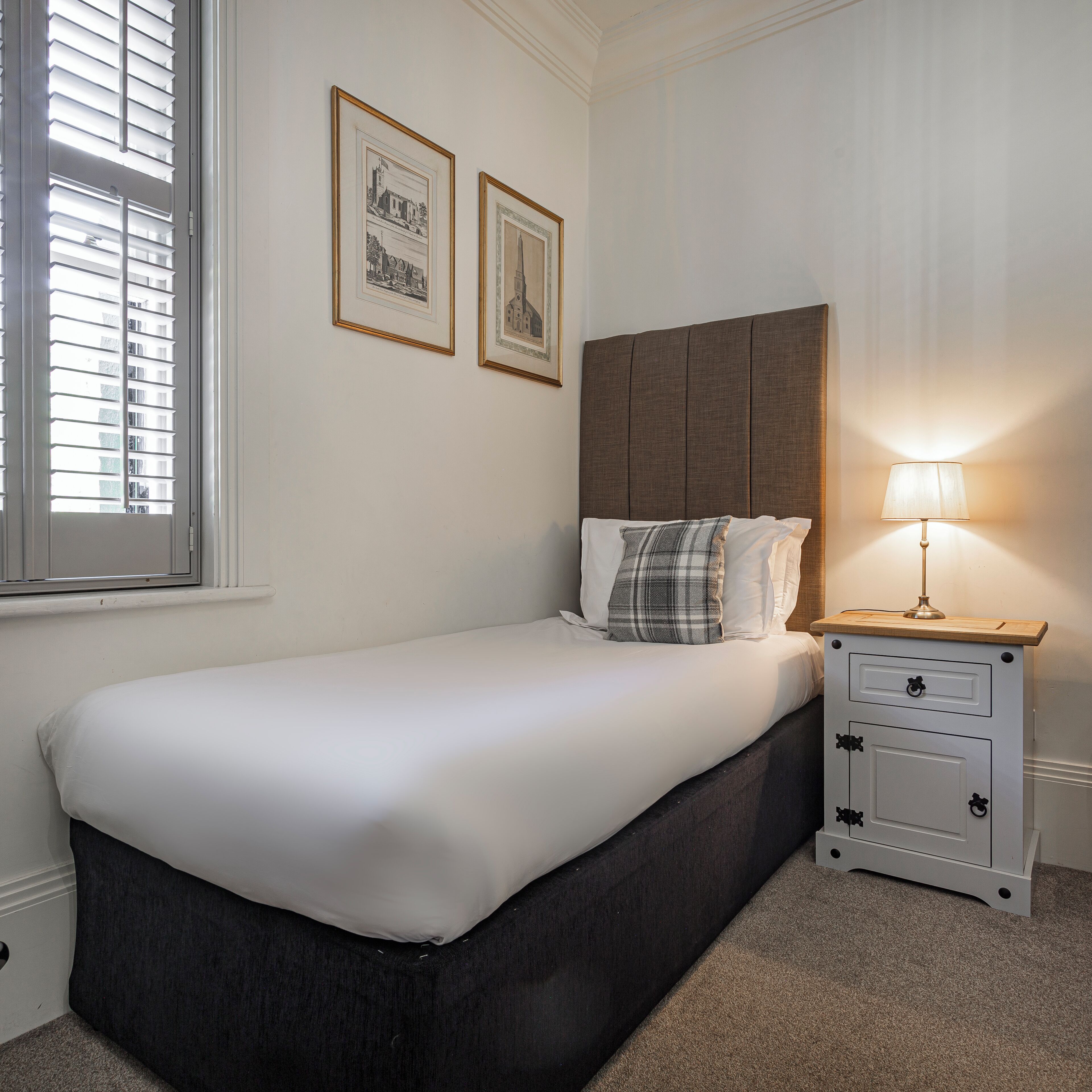 A bedroom with a bed, a nightstand, a lamp, and two framed pictures on the wall.