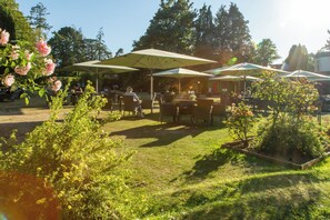 An outdoor seating area with tables and chairs under umbrellas, surrounded by greenery and trees. - Forest Park Country Hotel & Inn, Brockenhurst, New Forest (Brockenhurst)