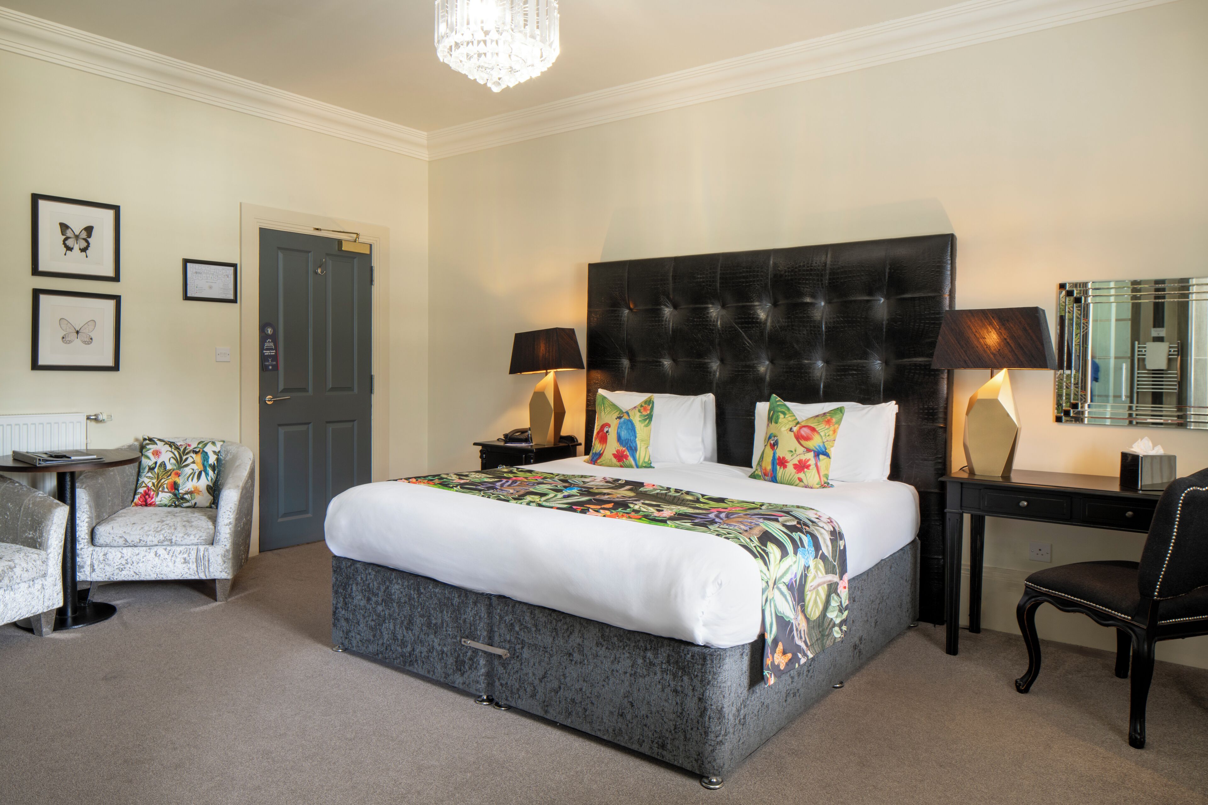 A hotel room with a large bed, two bedside tables, a desk, a chair, and a door.