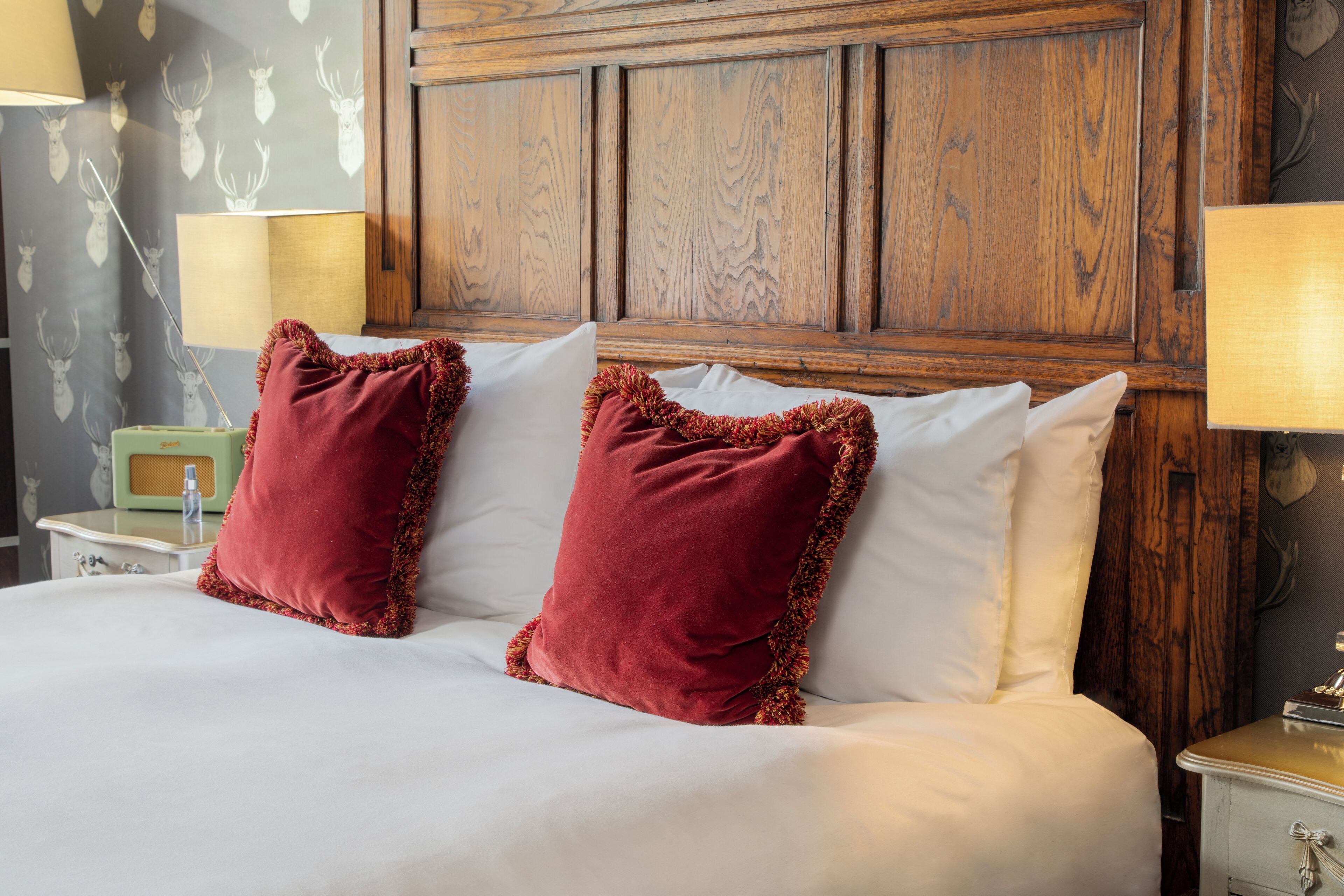 A bed with white and red pillows, a wooden headboard, and a nightstand with a lamp.