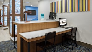A hotel reception desk with a computer, two chairs, and a colorful striped wall art piece.