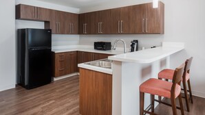 A modern kitchen with wooden cabinets, a black refrigerator, a microwave, and a white countertop.