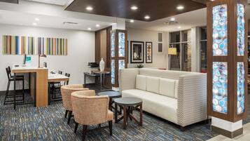 A modern hotel lobby with a seating area, a reception desk, and a large window with decorative glass panels.