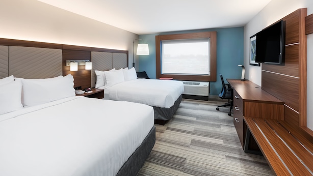 A hotel room with two beds, a desk, a TV, and a large window.